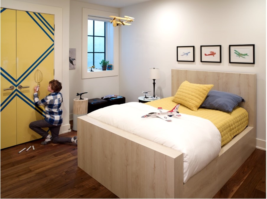 Kids bedroom with child writing on closet doors in Chrome Yellow and Matrix Blue Formica Laminate with double bed in Planked Raw Oak Formica Laminate with yellow, blue and white bedding