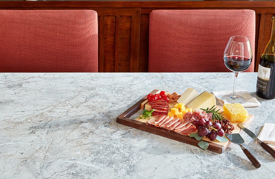 White marble Formica laminate dining table with wine and cheese surrounded by orange chairs