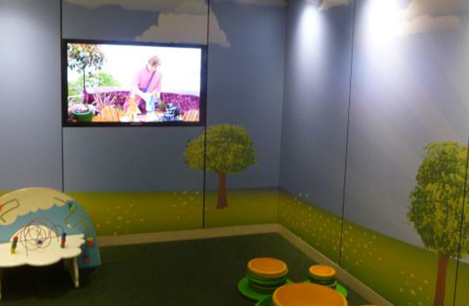 Zona de juegos para niños con juguetes, televisión y paneles personalizados de Formica Envision con árboles, hierba y cielo