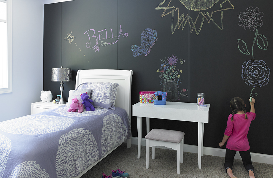 Niña dibuja en la pared de la recámara de las Superficies para Escribir Formica F3037 Black ChalkAble cerca de la cama y del escritorio.