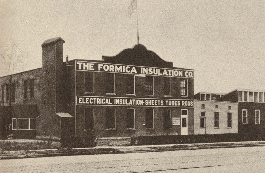 Una imagen histórica en blanco y negro de una fábrica de ladrillos con el nombre ‘The Formica Insulation Co.’ sobre el edificio
