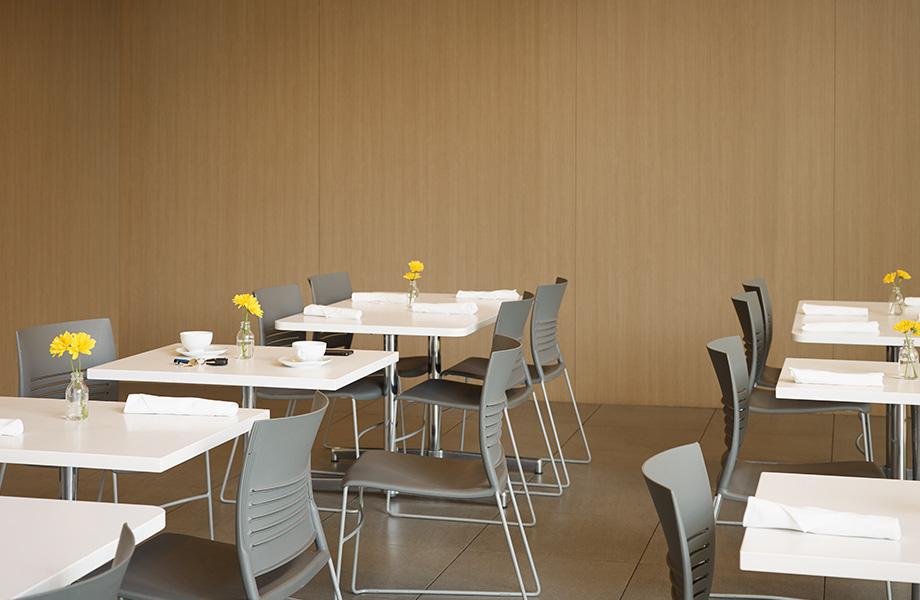 Restaurant avec panneaux muraux en stratifié de marque Formica Lisière de Pacanier et tables blanches en Surface Solide Everform Arctique avec chaises grises