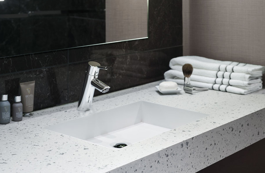 Meuble-lavabo d'une salle de bain d'hôtel avec comptoirs écoresponsables en 8812-PA Papier Terrazzo Teinté avec miroir, serviettes et articles de toilette à proximité