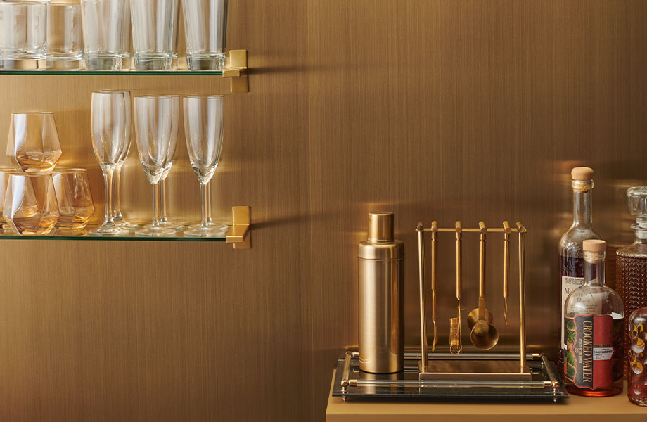 Bouteilles, verres et accessoires de bar devant un mur d’accent en stratifié métallique Homapal Laiton Huilé Ciré 