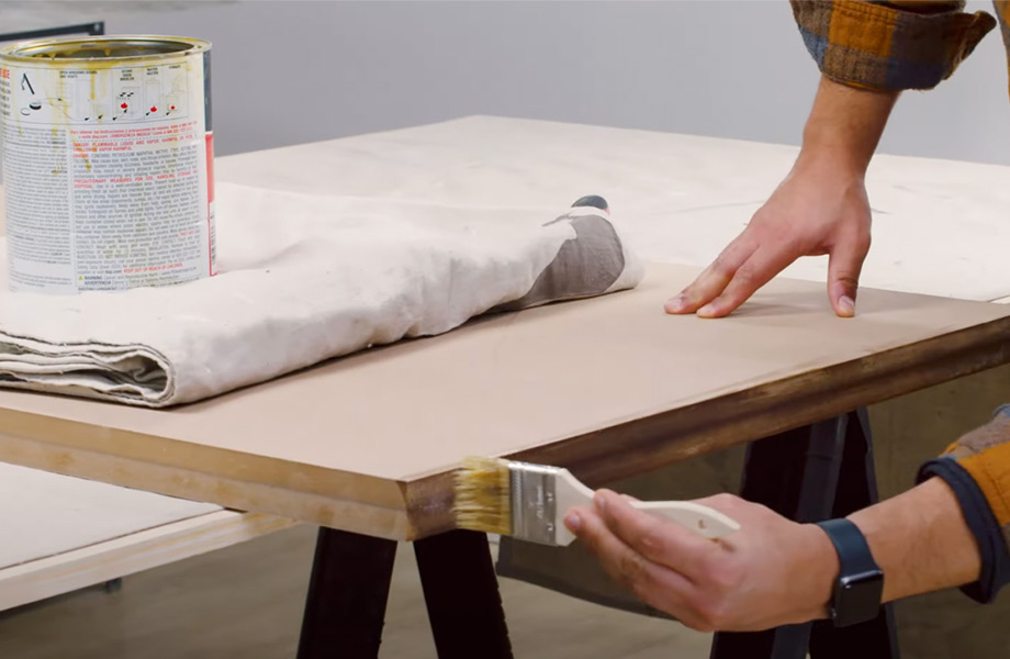 Une personne utilise un pinceau pour appliquer de l’adhésif sur l’arête d’une table. 